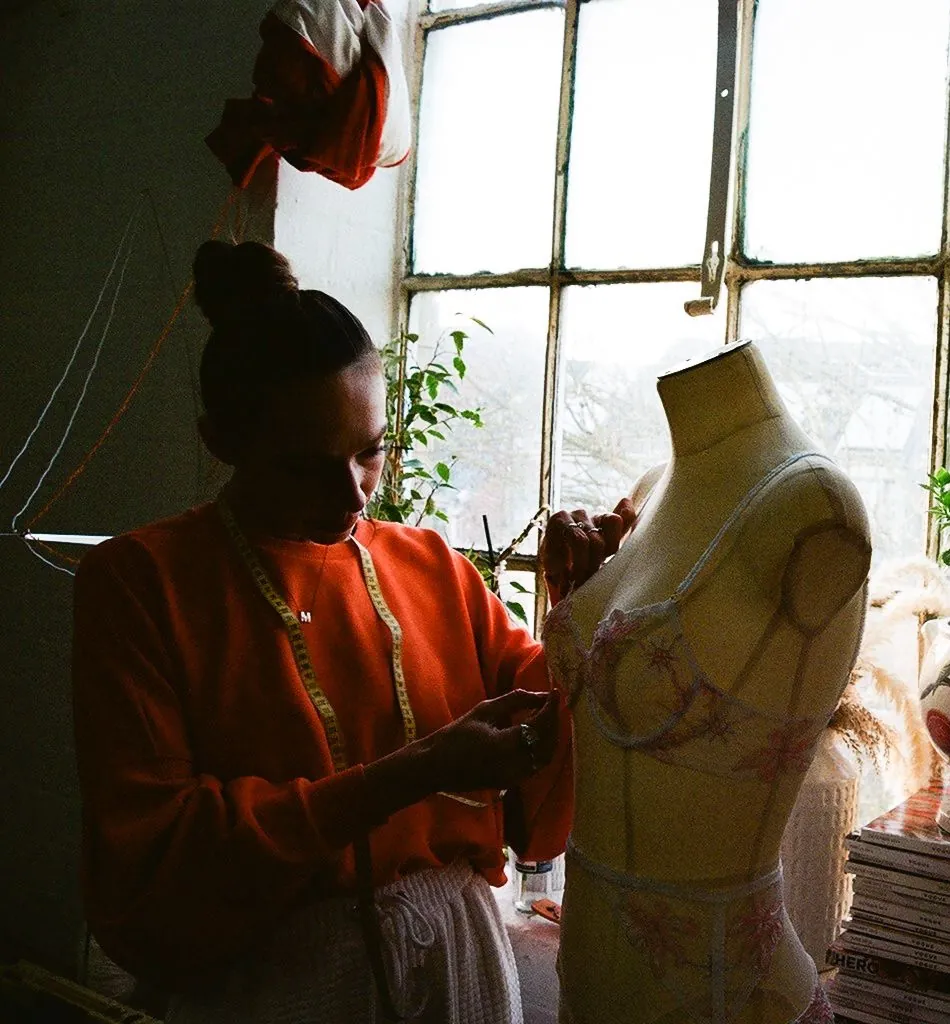 Designer fitting a hand-embellished lingerie sample on a tailor's mannequin in a sunlit Leicester studio